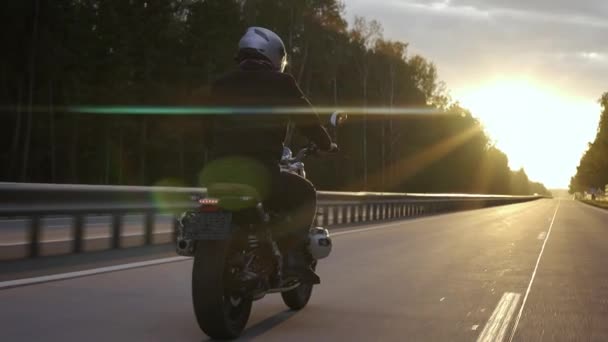 Uomo in sella alla moto scrambler in autostrada attraverso il bosco al tramonto — Video Stock