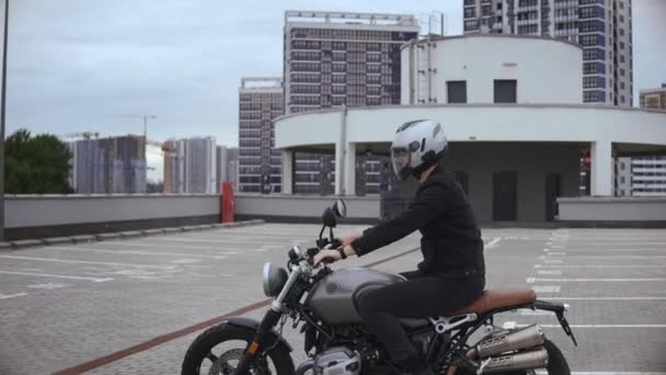 Człowiek zaczyna jeździć na motocyklu scrambler na szczycie wielopoziomowego parkingu — Wideo stockowe