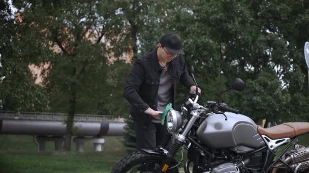 Giovane uomo pulire la sua moto scrambler in pelle con un panno sulla strada — Video Stock