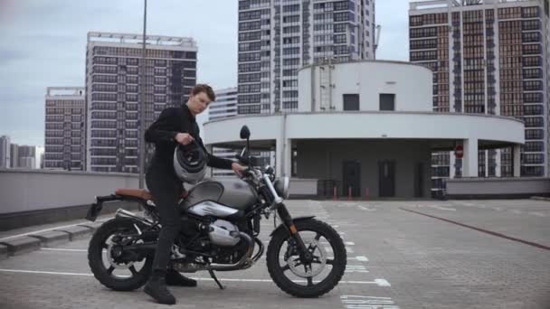 Чоловік носить шолом і починає мотоцикл на вершині багаторівневої парковки — стокове відео