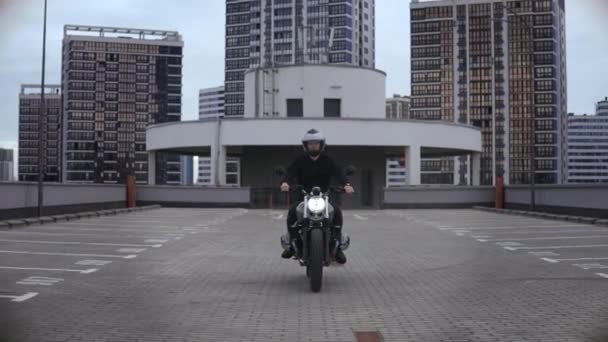 Muž na koni scrambler motocykl na vrcholu multi-level parkování ve městě — Stock video