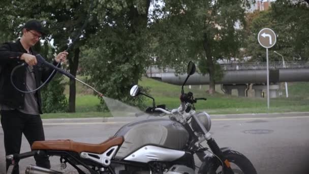 Jovem lavando sua moto scrambler com mangueira de água na rua — Vídeo de Stock