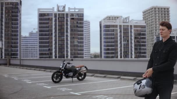Facet nosi kask motocyklowy na szczycie parkingu, przed motocyklem — Wideo stockowe