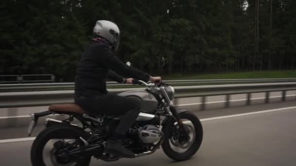 Man ridning scrambler motorcykel på motorvägen genom höstskogen — Stockvideo