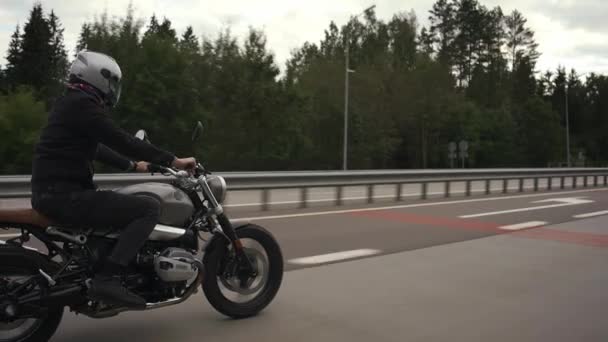 Человек едет скремблер мотоцикл по шоссе через осенний лес — стоковое видео
