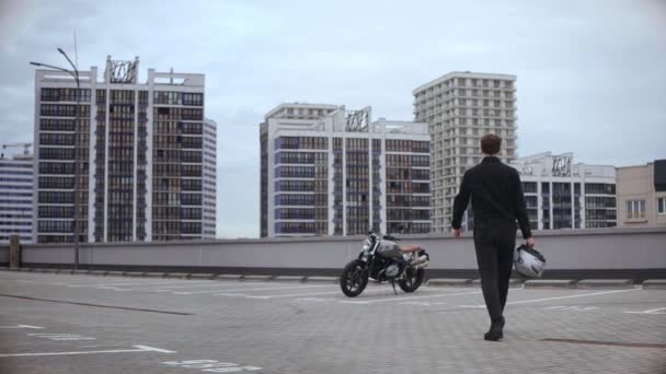 Mężczyzna podchodzi do motocykla i nosi kask na szczycie wielopoziomowego parkingu — Wideo stockowe