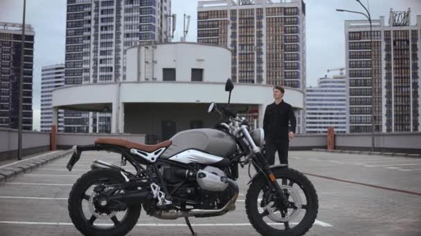 Man kommer till scrambler motorcykel och bär hjälm på toppen av flera nivåer parkering — Stockvideo