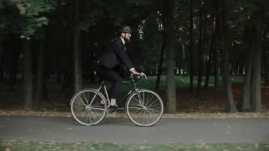 Şehir parkında bisiklet süren genç bir adam. Takım elbise ve kask giyiyor.