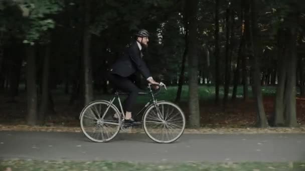 Jovem andando de bicicleta no parque da cidade vestindo terno de negócios e capacete, vista lateral — Vídeo de Stock