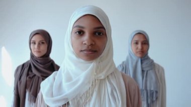 Üç Müslüman kız, parlak stüdyoda kameraya bakıp gülümsüyor.