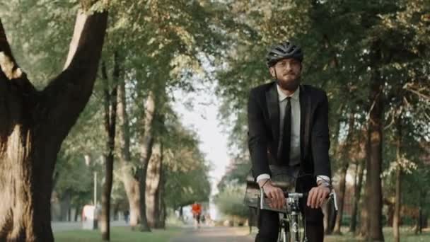 Homme d'affaires en vélo dans le parc de la ville en costume et casque, vue de face — Video