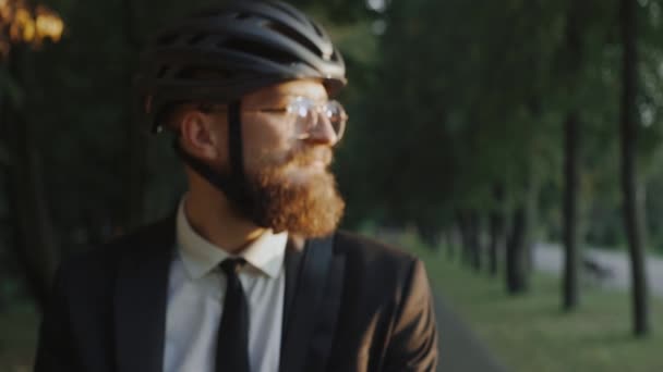 Affärsman i cykelhjälm stående i parken vid solnedgången tittar på kameran — Stockvideo