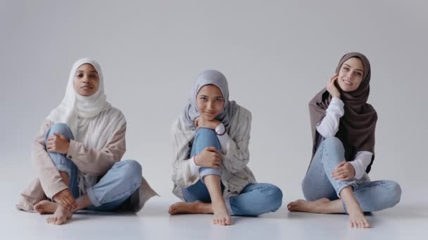 Tiga gadis muslim duduk bersama tersenyum dan tertawa di studio putih cerah — Stok Video