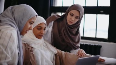 Üç Müslüman kız kanepede oturmuş dizüstü bilgisayara bakıp gülümsüyor ve gülüyor.