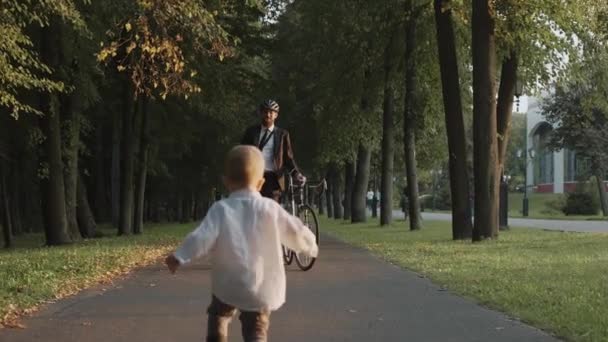 Baby kör för att träffa sin pappa efter jobbet, affärsman med cykel i stadsparken — Stockvideo