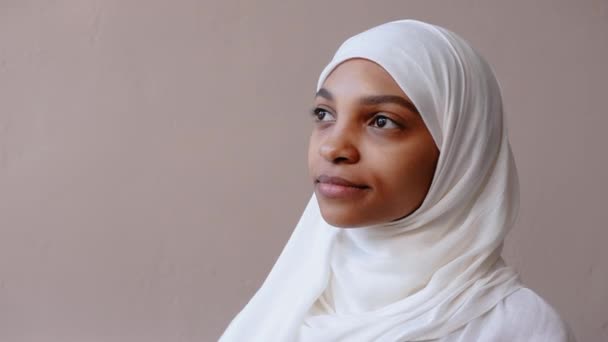 Νεαρή μουσουλμάνα με λευκή μαντίλα κοίτα την κάμερα και χαμογέλα πλατιά — Αρχείο Βίντεο