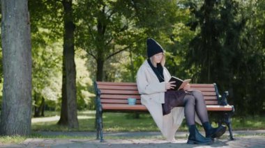 Sonbaharda parkta bankta oturmuş kitap okuyor ve gülümsüyor.