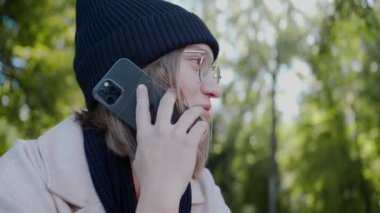 Sonbaharda parkta bankta oturan, telefonla konuşan ve gülümseyen genç bir kız.