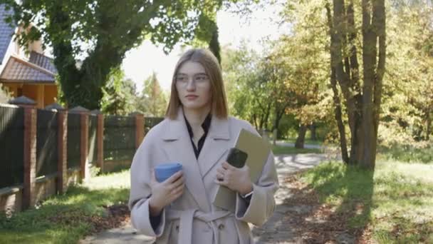 Junges Mädchen spaziert an einem sonnigen Herbsttag im Mantel durch die grüne Nachbarschaft — Stockvideo