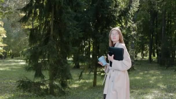 Chica caminando en el parque de la ciudad en un día soleado de otoño, bebiendo de una copa ecológica — Vídeos de Stock