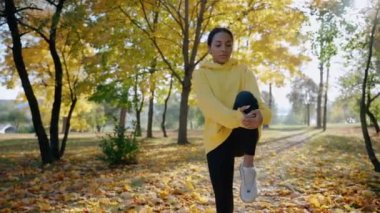 Kız sonbaharda parkta sabah koşusundan önce egzersiz ve esneme hareketleri yapıyor.