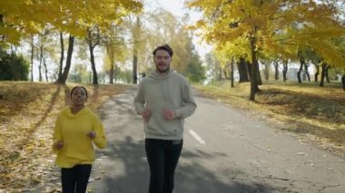 Kadın ve erkek sonbaharda parkta koşuyor, konuşuyor ve gülümsüyor.