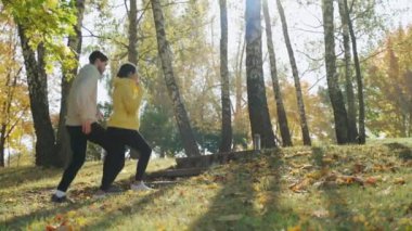 Genç bir adam ve kadın güneşli bir sonbahar sabahı parkta atlama egzersizi yapıyorlar.