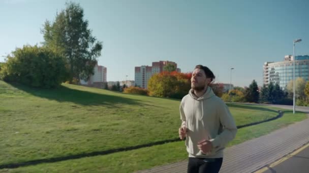 Mann läuft an sonnigem Herbstmorgen auf Joggingstrecke am Stadtpark, Seitenansicht — Stockvideo