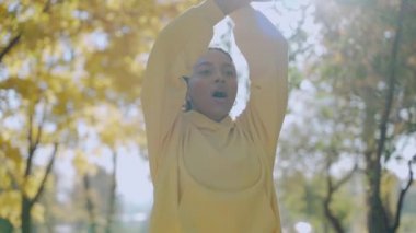 Kız sonbaharda parkta sabah koşusundan önce egzersiz ve esneme hareketleri yapıyor.