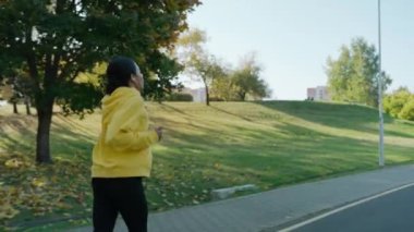 Güneşli bir sonbahar sabahında şehir parkında kulaklıkla koşan bir kız.