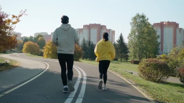 Чоловік і жінка бігають на трасі в парку восени, розмовляючи і посміхаючись — стокове відео