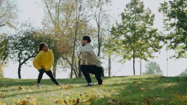 Homem e mulher se exercitando e se alongando antes da corrida matinal no parque no outono — Vídeo de Stock