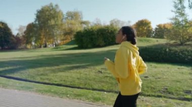 Güneşli bir sonbahar sabahında şehir parkında kulaklıkla koşan bir kız.