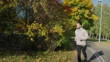 Güneşli bir sonbahar sabahı şehir parkında koşan bir adam.
