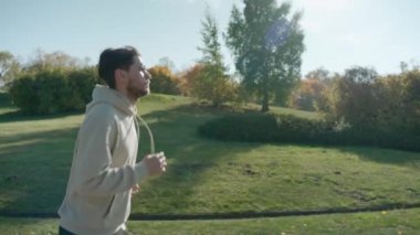 Güneşli bir sonbahar sabahında, şehir parkında koşan bir adam.