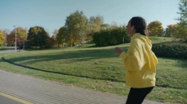 Güneşli bir sonbahar sabahında şehir parkında kulaklıkla koşan bir kız.