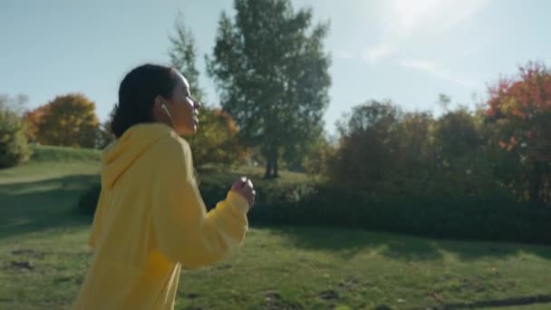 Mädchen läuft an einem sonnigen Herbsttag mit Kopfhörern auf Gehweg im Stadtpark — Stockvideo