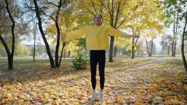 Menina fazendo salto jack e alongamento antes da corrida da manhã no parque no outono — Vídeo de Stock