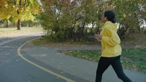 Mädchen läuft an sonnigem Herbstmorgen mit Kopfhörern auf Gleis im Stadtpark — Stockvideo