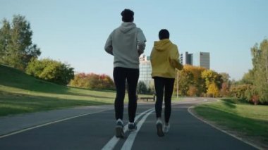 Güneşli bir sonbahar sabahı şehir parkında koşan bir adam ve kadın.