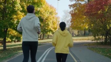 Güneşli bir sonbahar sabahı şehir parkında koşan bir adam ve kadın.