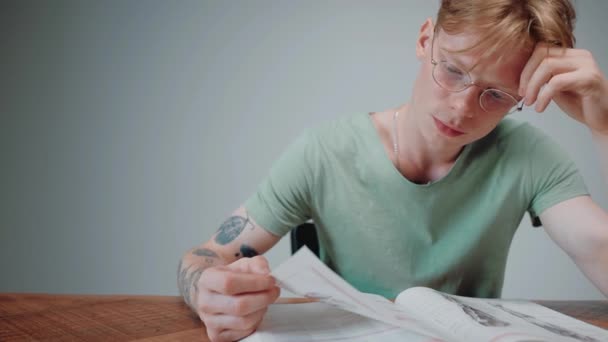 Szemüveges férfi tanul és stresszel, tankönyvet olvas az üres szürke szobában. — Stock videók