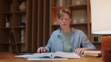 Gözlüklü genç adam sıcak ahşap odada bir şeyler öğrenmeye çalışıyor ve strese giriyor.