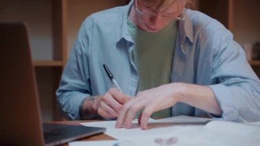 Genç adam ders kitabını karıştırıyor, notlar yazıyor, ödev yapıyor.