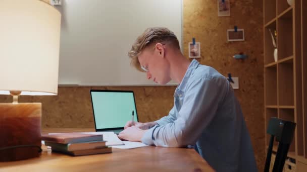 Молодий чоловік вчиться вдома, відмовляється знімати окуляри і лежить на столі — стокове відео