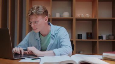 Genç adam aktif olarak laptopta yazıyor, evden çalışıyor.