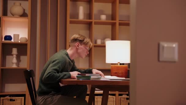Guy studiert zu Hause, hat einen Videoanruf auf einem Laptop, durchsucht Lehrbücher — Stockvideo