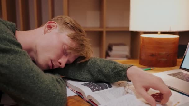 El tipo se quedó dormido mientras hacía los deberes en la mesa, acostado en los libros, vista lateral — Vídeos de Stock