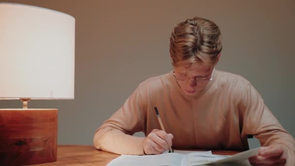 Jovem estudando em casa escrevendo em suas anotações, lendo um livro na mesa — Vídeo de Stock