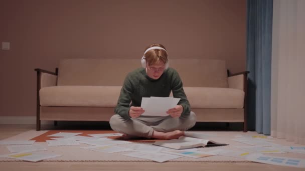 Stressad kille sitter på golvet full av papper och ger upp, lutar sig mot soffan — Stockvideo